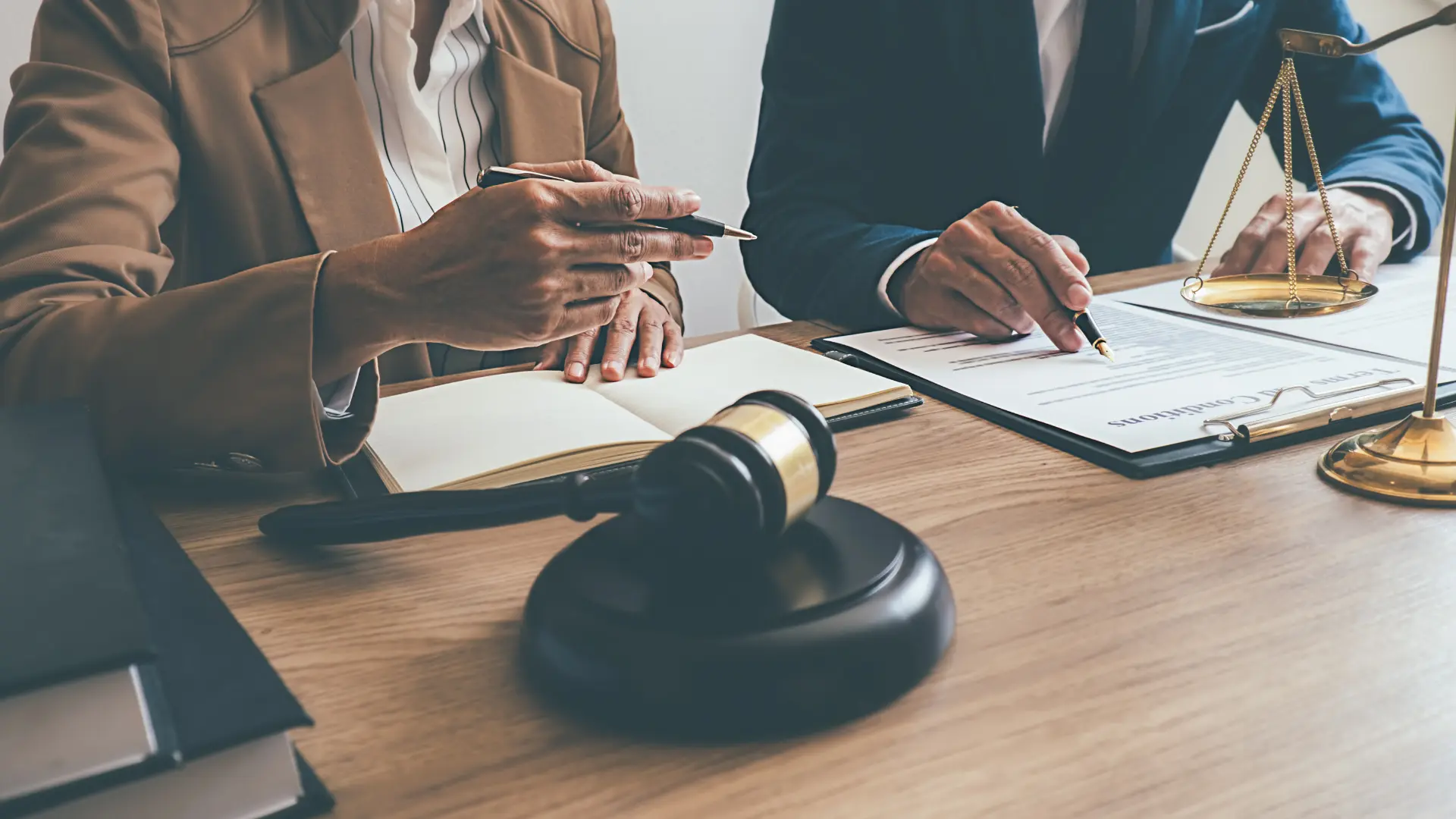 Two lawyers in business attire seated at a desk with a gavel and a pen, engaged in a professional discussion.